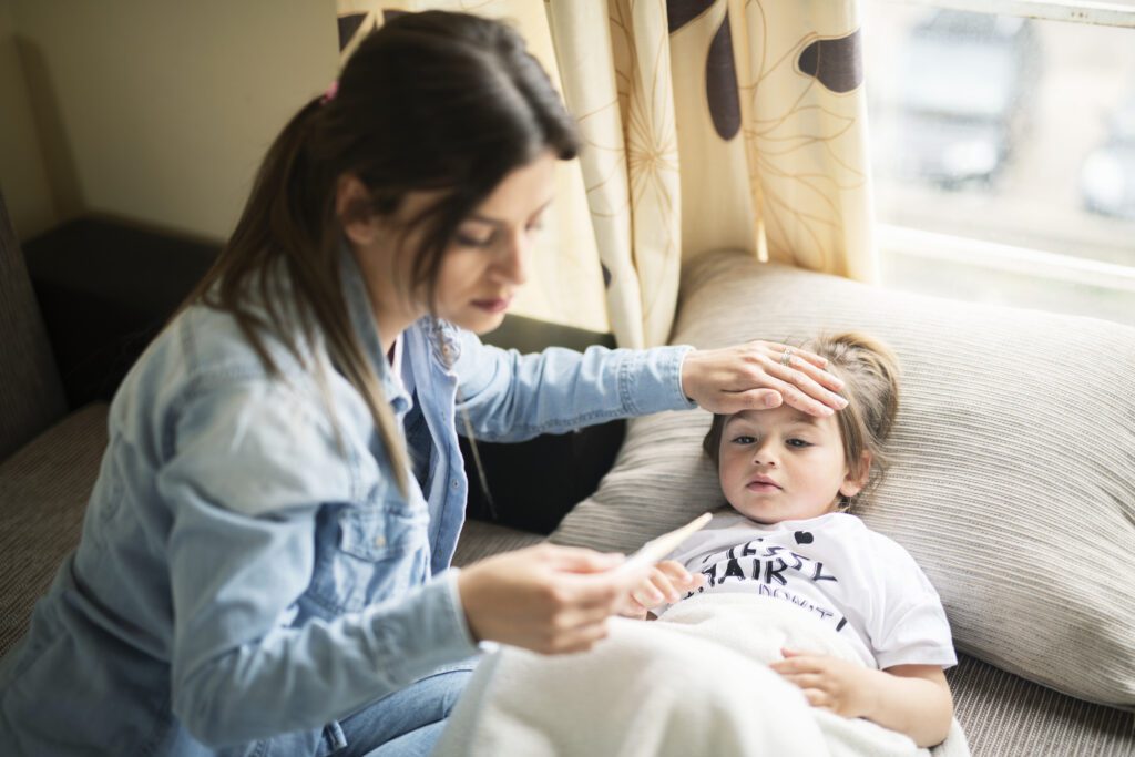 A sick child at home from school with their parent checking their temperature and worried that they have RSV, flu or Covid19.