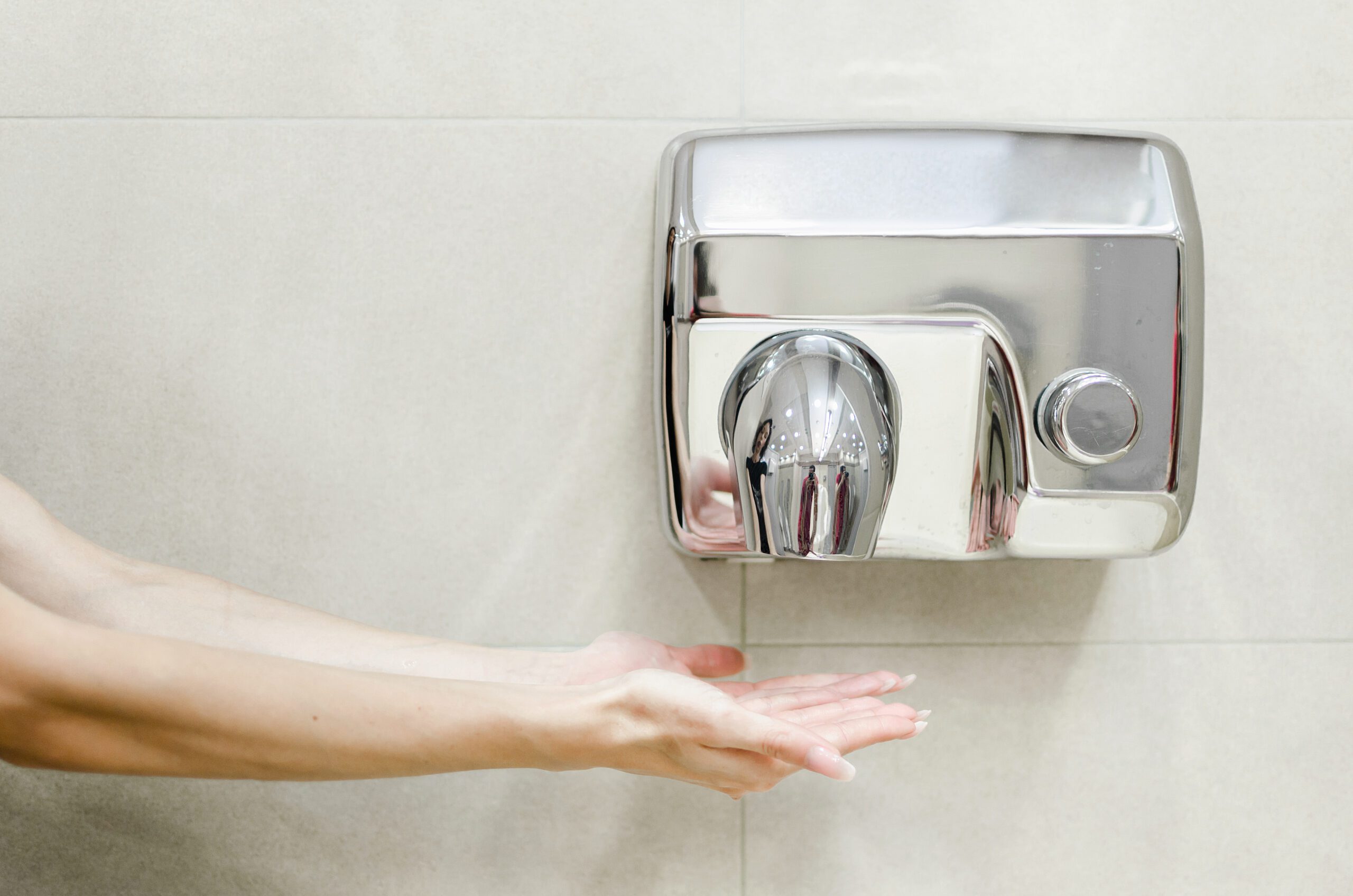 Woman using generic hand dryer in public bathroom